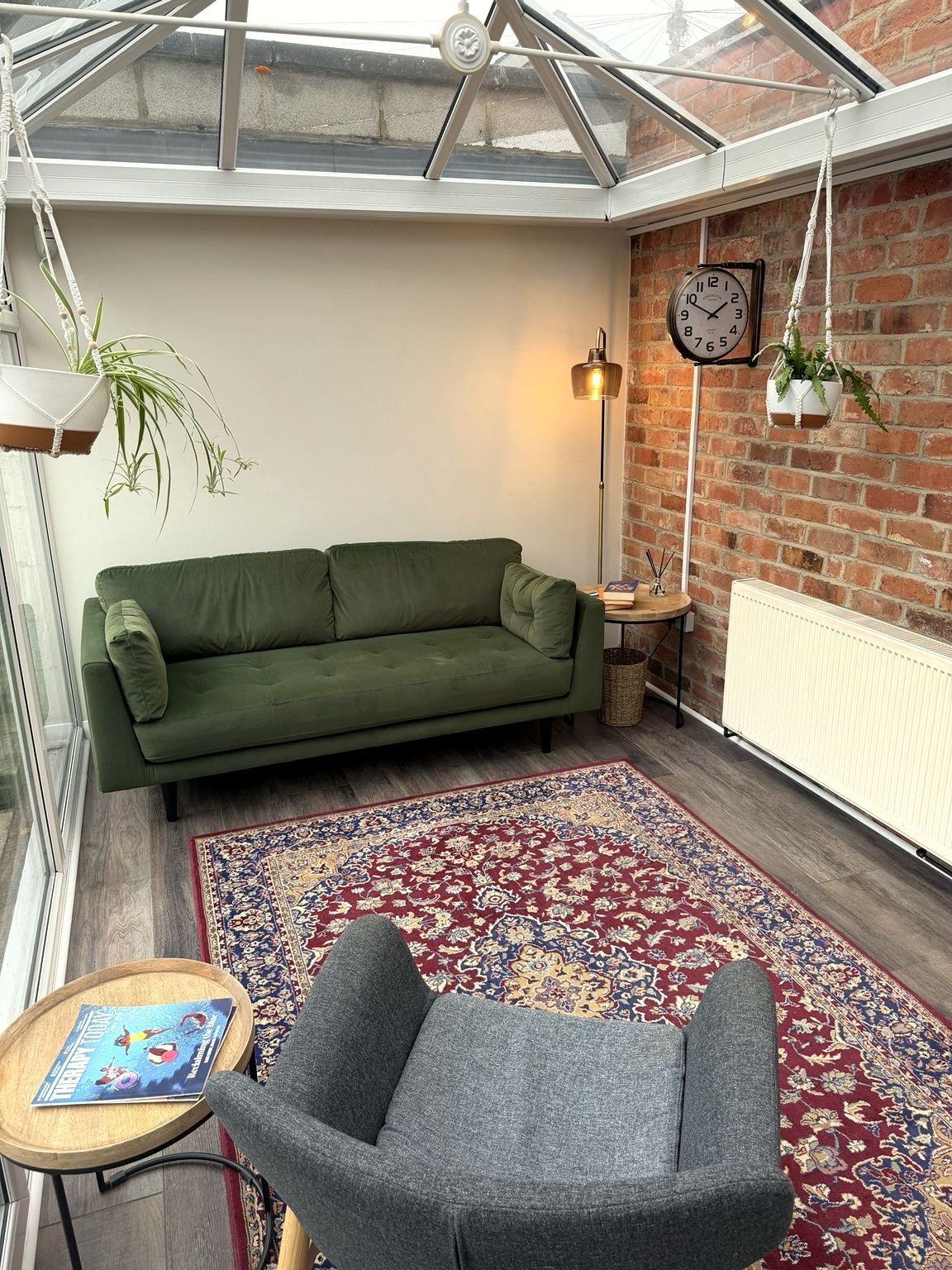 The garden room seating — green sofa and armchair on a patterned rug against a brick wall