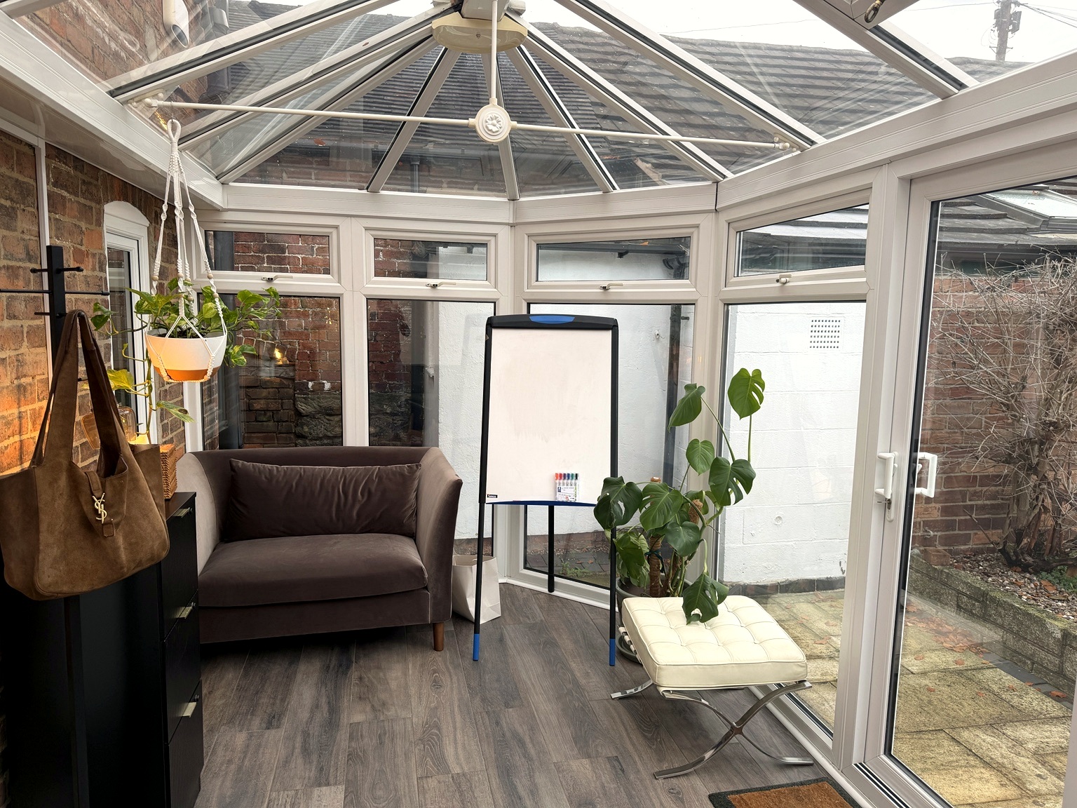 The garden room set out for group work — loveseat, cream leather chair, whiteboard and plants