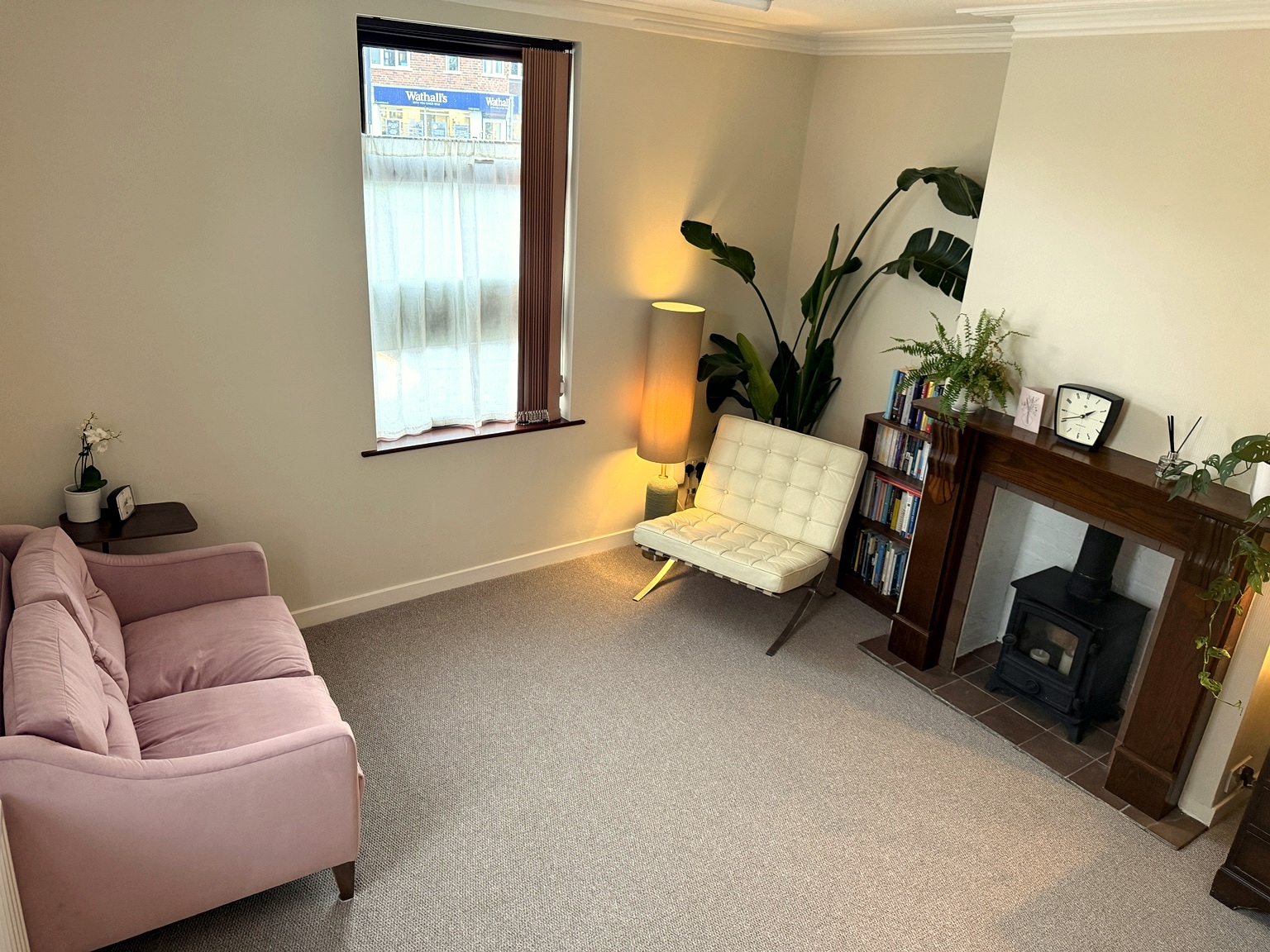 The therapy room — a bright, welcoming space with a velvet sofa, leather chairs and a wood-burning stove