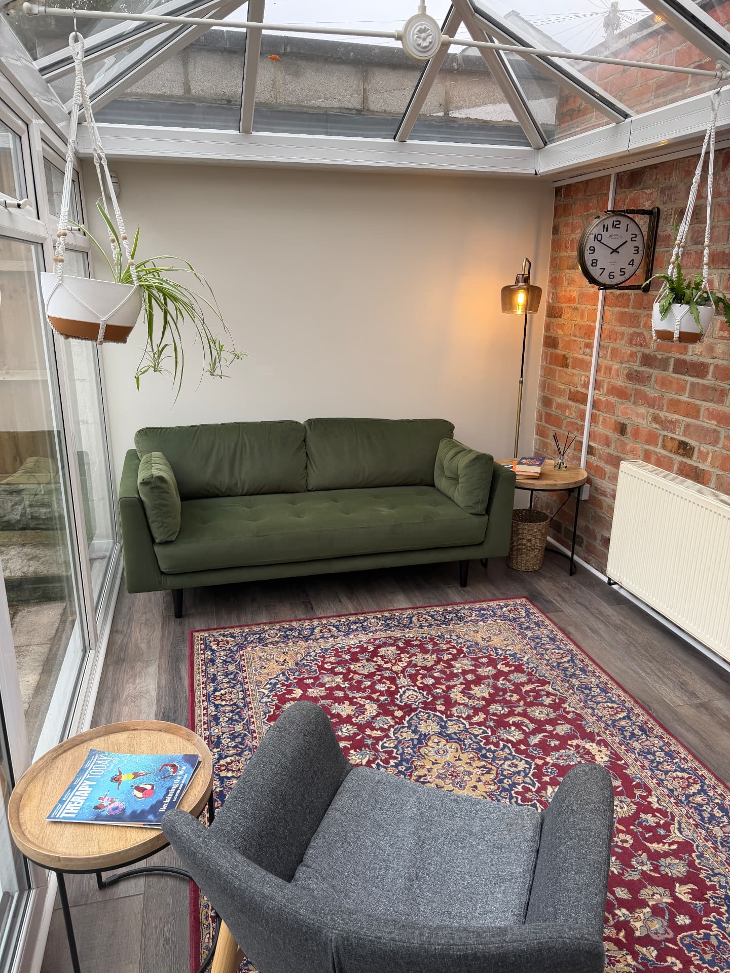 The garden room — a green velvet sofa and hanging plants beneath a glass roof