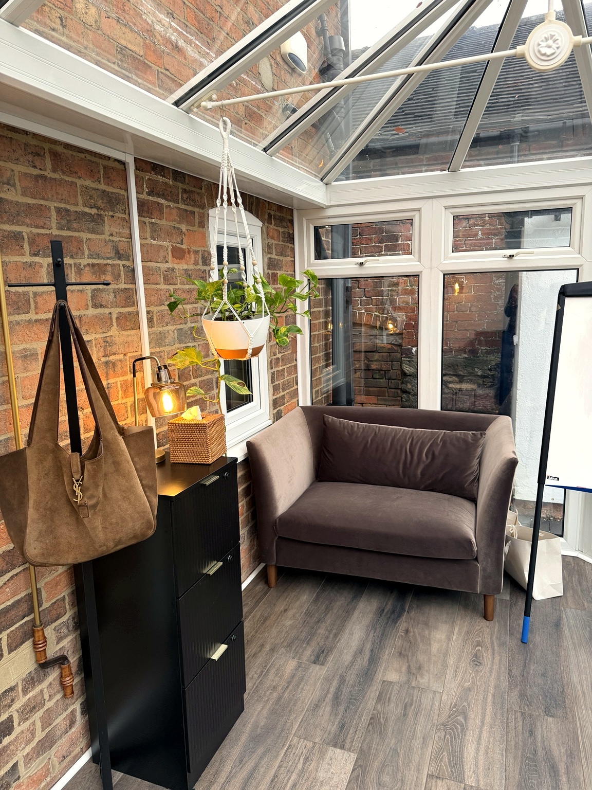 A quiet corner of the garden room — a brown velvet loveseat and warm lamp light